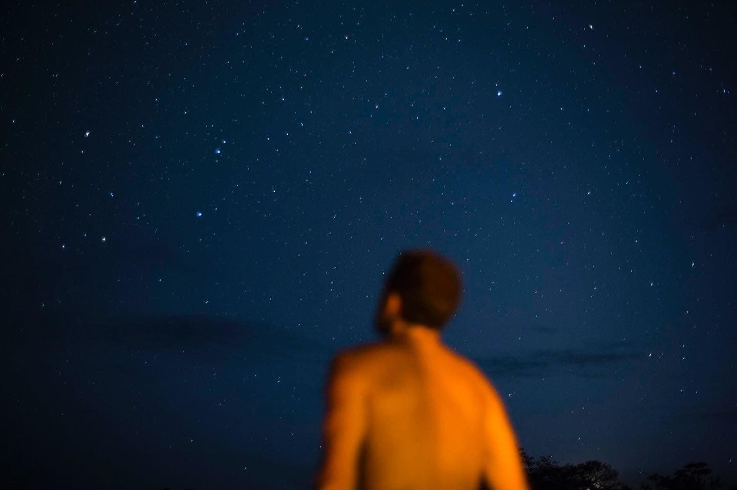 No city lights, no distractions. Just you and the whole southern sky. A person lit by warm firelight gazes up at a brilliant star-filled sky during an Amazon jungle cruise Brazil night aboard the river