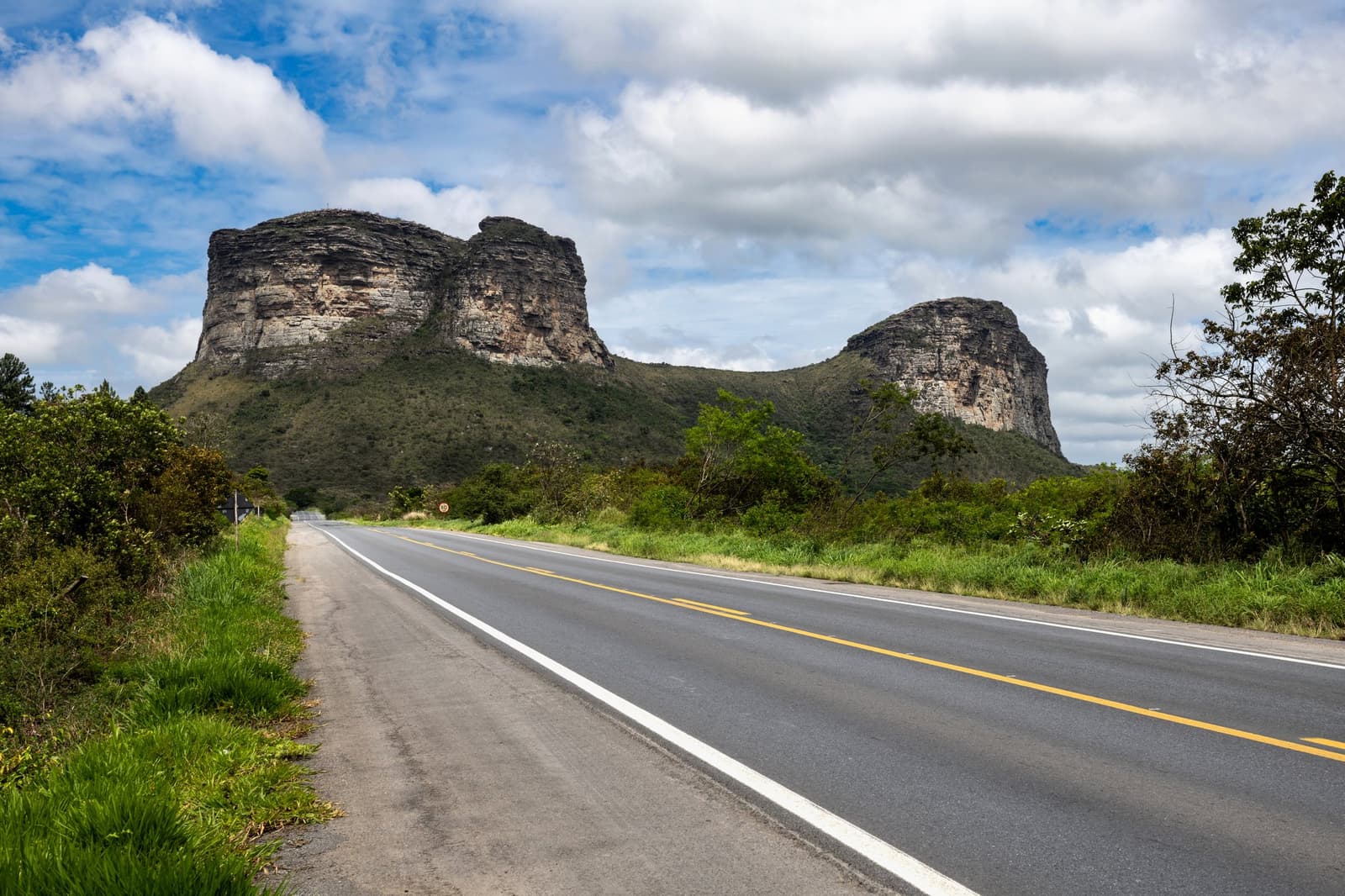 The road tells you where you're going; the mesas remind you it's worth it. An empty two-lane road leads straight toward two flat-topped sandstone mesas rising above green scrubland on a Chapada Diamantina Tour