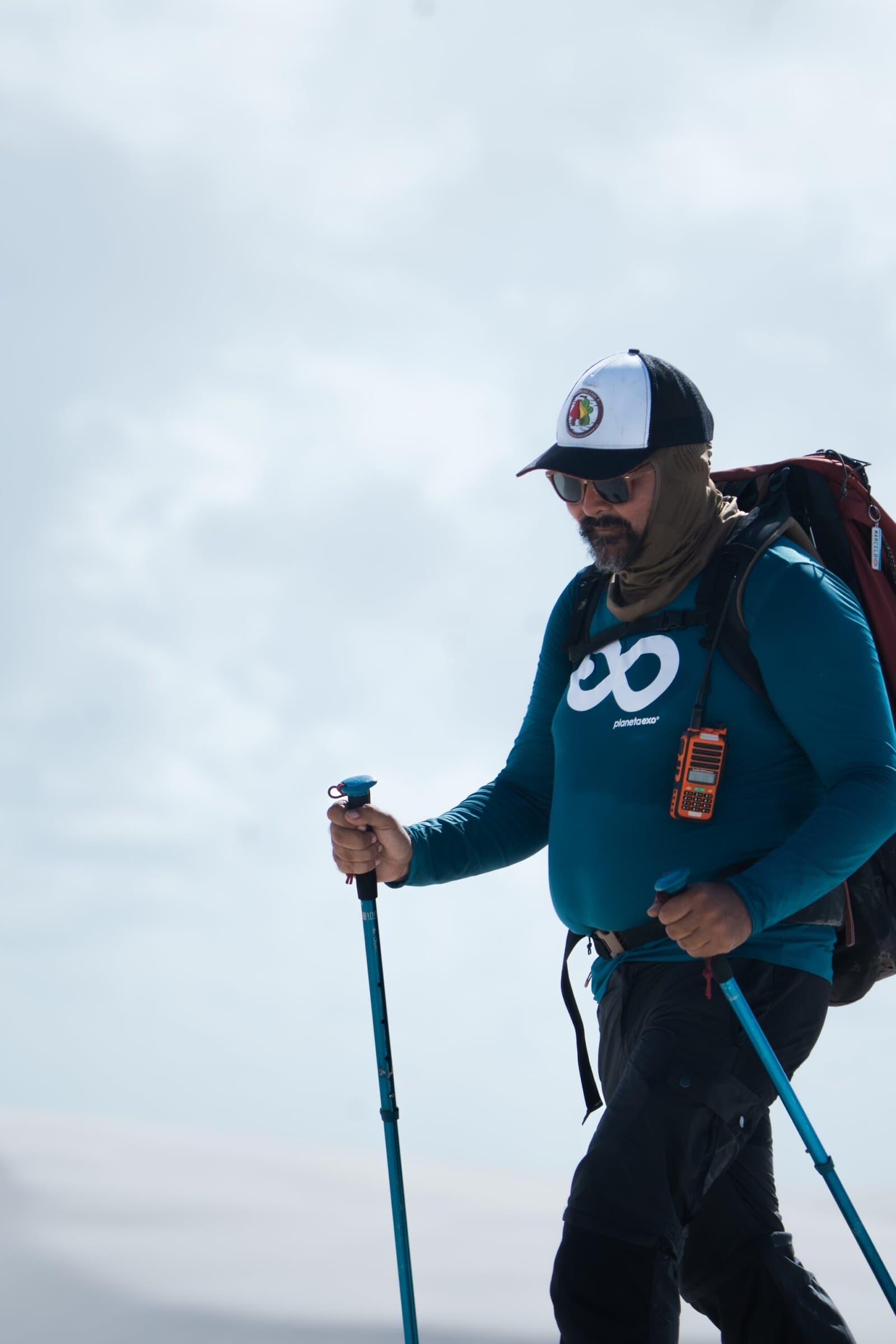 Every good trail deserves someone who actually knows where it leads. A PlanetaEXO guide in full trekking gear, holding hiking poles and carrying a large backpack with a radio clipped to the chest strap, during a Lençóis Maranhenses hike