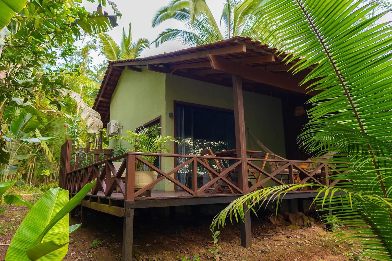 Palms so close you could shake hands with them from the deck. A green-walled Amazon boutique lodge bungalow with a raised wooden deck and cross-railed balustrade, surrounded by palm fronds, banana leaves and tropical forest canopy