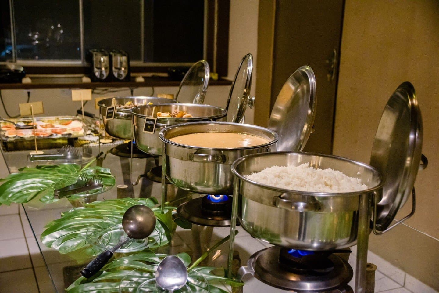 Hot food, blue flames, and a generous spread after a long day in the field. Stainless steel chafing dishes with rice and a warm sauce kept hot over blue flames at a lodge buffet dinner, part of the full-board budget Pantanal tour experience