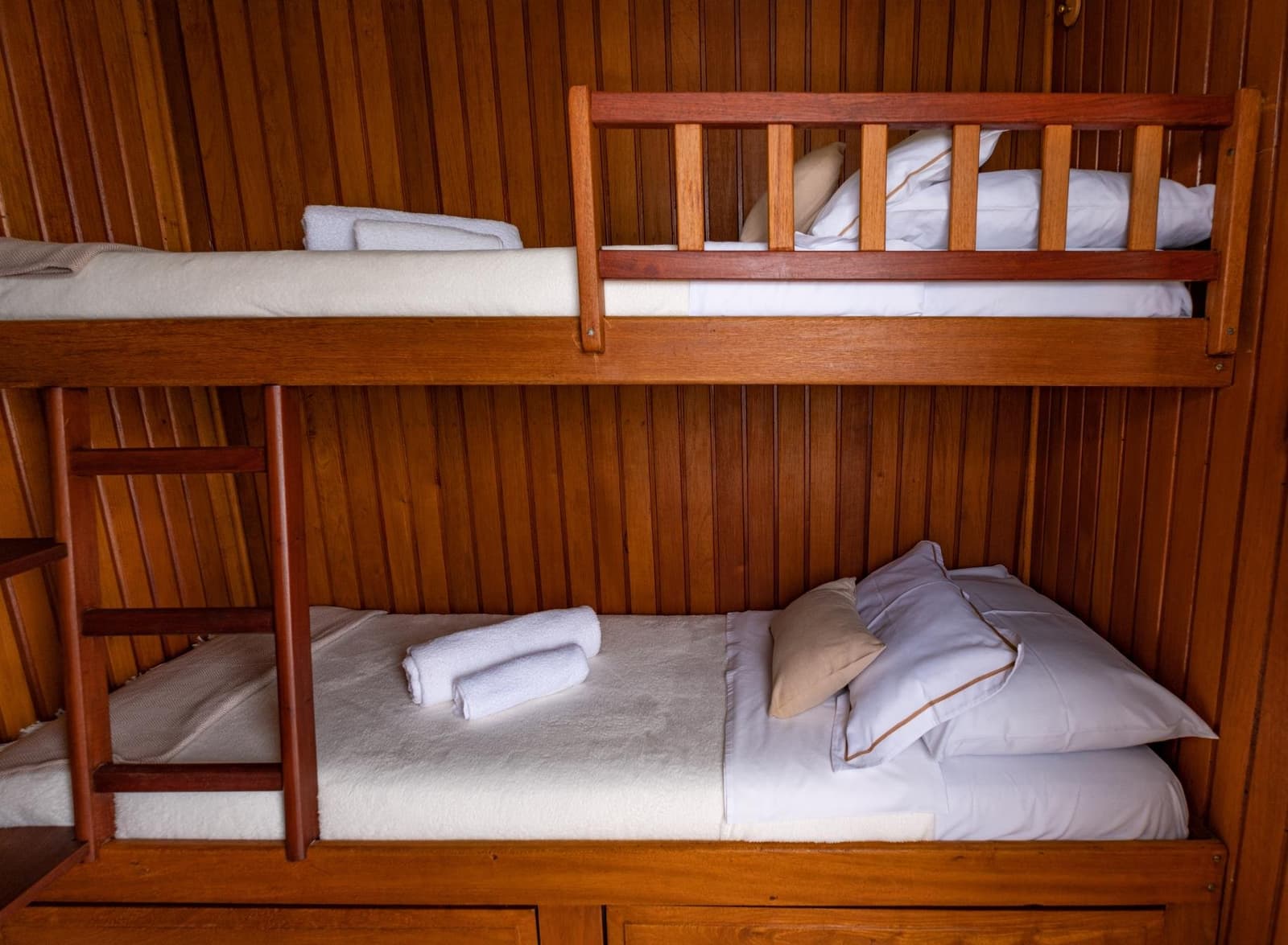 Compact, clean, and surprisingly comfortable, river life has its own rhythm. Neatly made wooden bunk beds with white linens, rolled towels, and grey pillows inside a timber-panelled cabin on an Amazon cruise from Alter do Chão