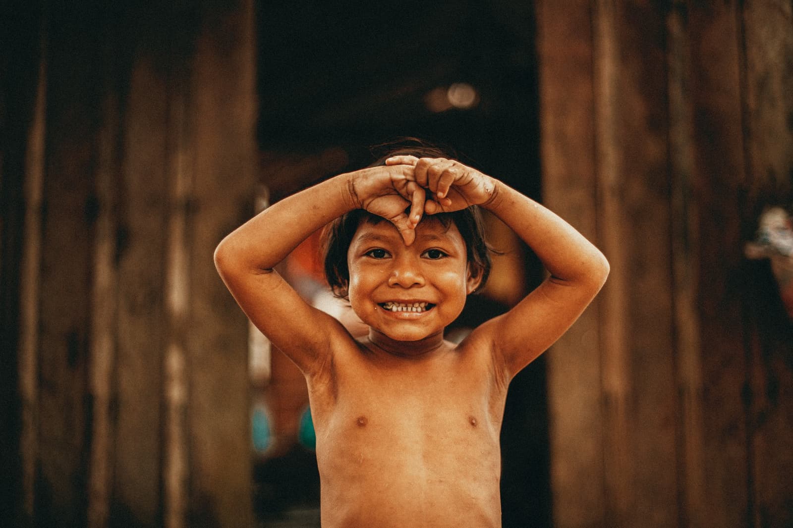 Some smiles you just can't plan for. A laughing child in a riverside community near Anavilhanas Jungle Lodge Brazil, hands raised playfully above their head in front of a wooden wall