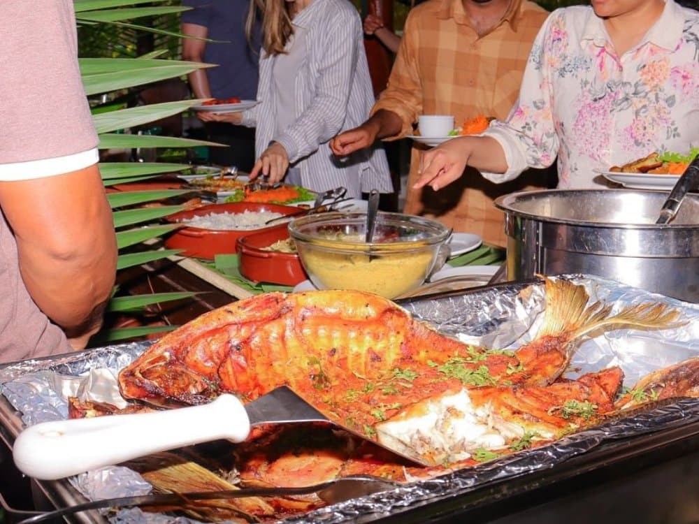 Fresh from the river â a whole roasted fish takes centre stage at the jungle buffet. A whole roasted fish garnished with herbs served on a foil tray at an outdoor buffet table on a brazilian amazon jungle tour, alongside rice, a golden sauce, and other dishes while guests help themselves