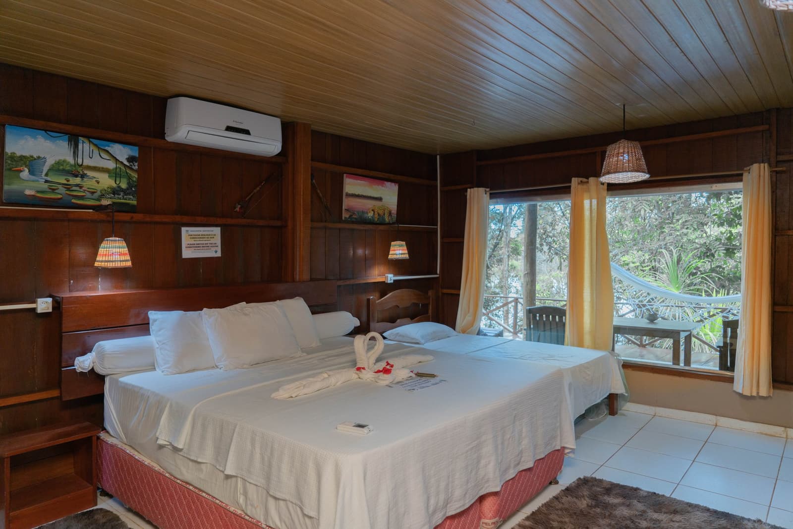 Towel-folded swans on crisp sheets, a hammock waiting just beyond the glass. Photo: Yuri Panichi A comfortable twin-bed lodge room with dark timber walls, wildlife artwork, woven lampshades, and a private balcony with a hammock overlooking lush rainforest â part of the brazilian amazon jungle tour experience