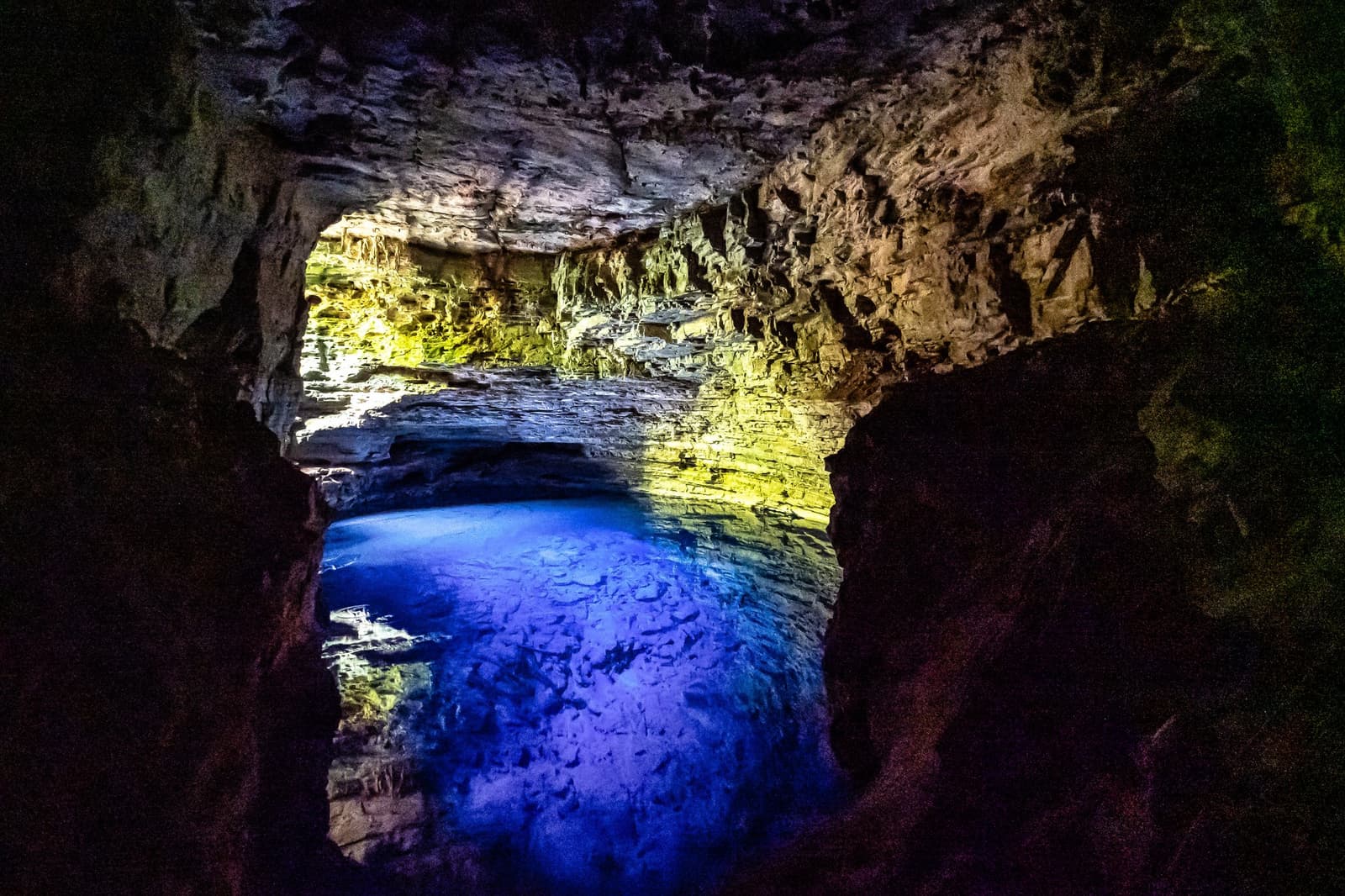 That shade of blue has no business being underground. Illuminated limestone cave interior with a vivid blue underground lake glowing beneath a rocky arch, a highlight of the chapada diamantina hike ending at Poço Azul