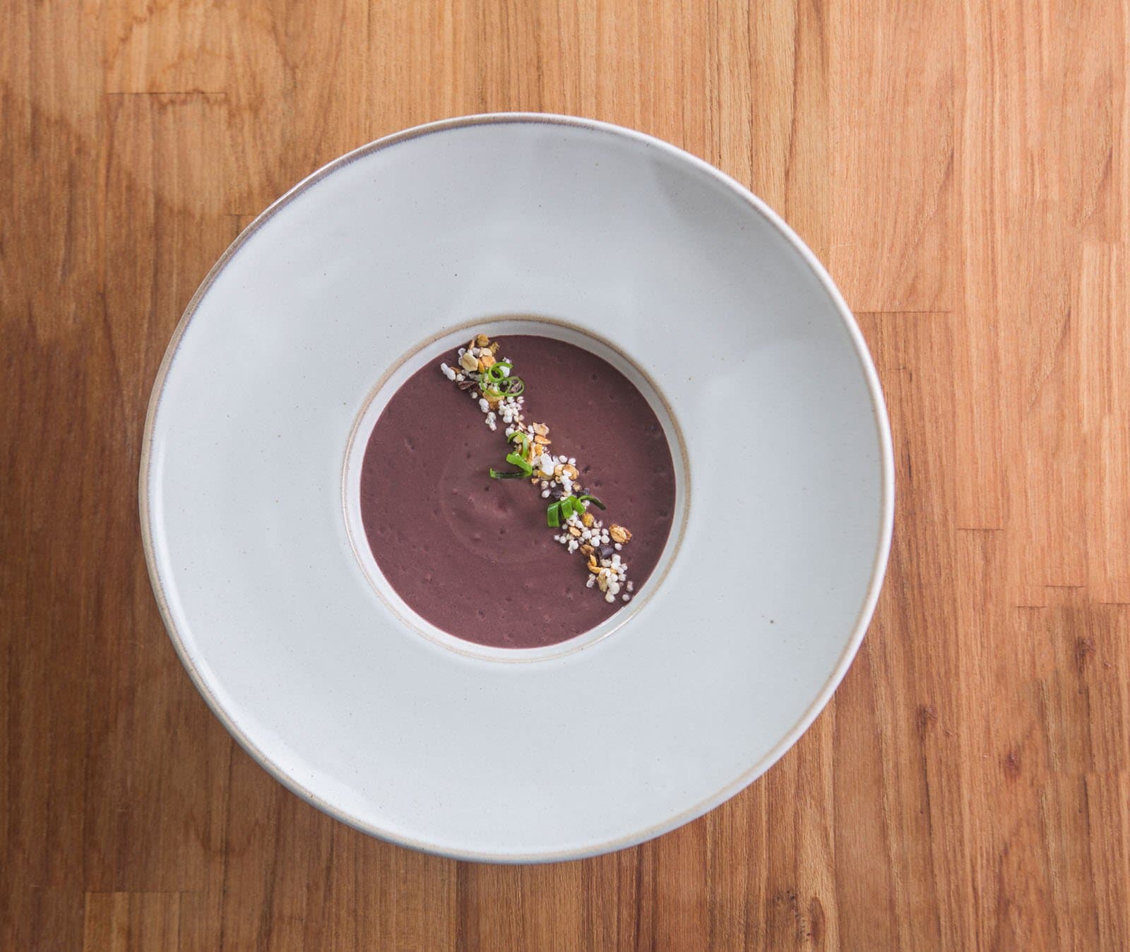 Simple ingredients, serious cooking, proof the rainforest larder runs deep. A smooth deep-purple cream soup served in a wide white ceramic bowl at Cristalino Jungle Lodge, garnished with a diagonal line of toasted grains, puffed seeds, and sliced spring onion