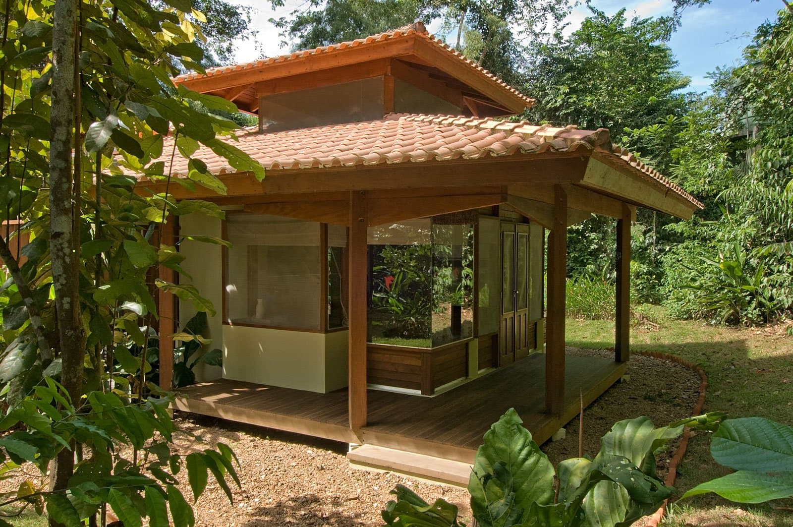 Your own patch of forest, with a roof over it and a cold drink nearby. A timber-framed bungalow with terracotta roof tiles and a wraparound hardwood deck at Cristalino Jungle Lodge, set among lush tropical garden greenery