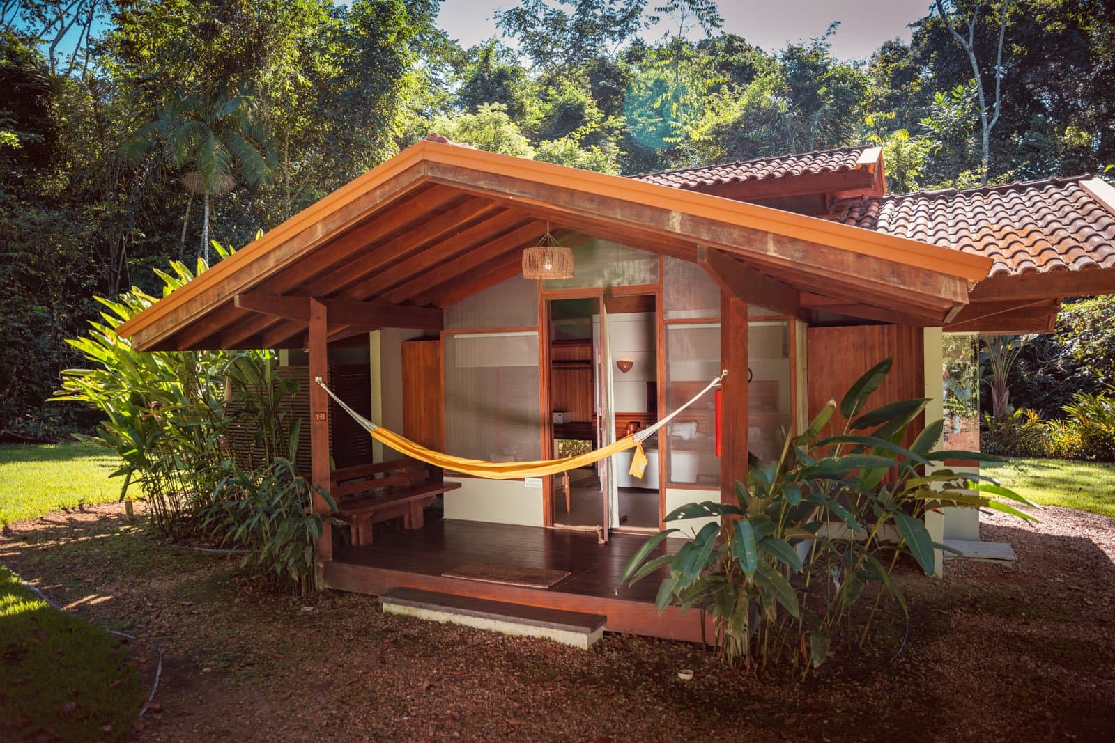 Your afternoon sorted: hammock, forest air, and nowhere else to be. A wooden bungalow at Cristalino Jungle Lodge with a yellow hammock strung across the covered veranda, surrounded by lush tropical greenery