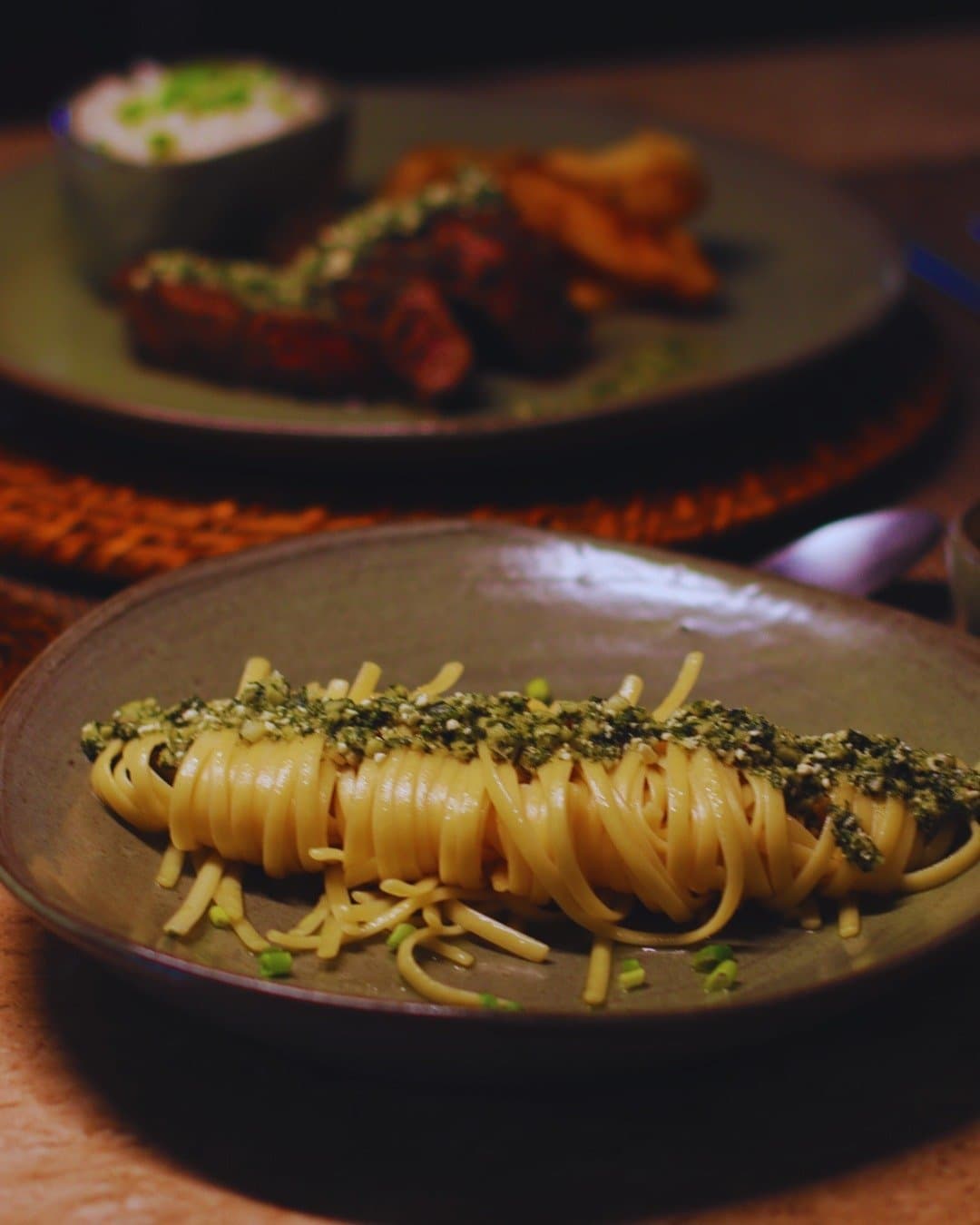Dinner in the jungle hits differently when the kitchen cares this much. A nest of linguine-style pasta topped with herb and seed crumble served on a rustic ceramic plate at Juma Amazon Jungle Lodge, with a plate of grilled meat blurred in the background