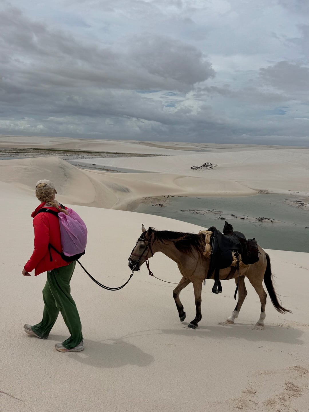 A traveler leads a horse on foot across the vast white dunes of Lençóis Maranhenses under a cloudy sky. A traveler leads a horse on foot across the vast white dunes of Lençóis Maranhenses under a cloudy sky.