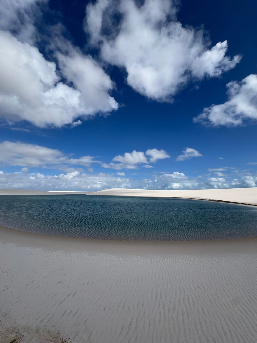 A turquoise rainwater lagoon nestled between white sand dunes under a bright blue sky in Lençóis Maranhenses. A turquoise rainwater lagoon nestled between white sand dunes under a bright blue sky in Lençóis Maranhenses.