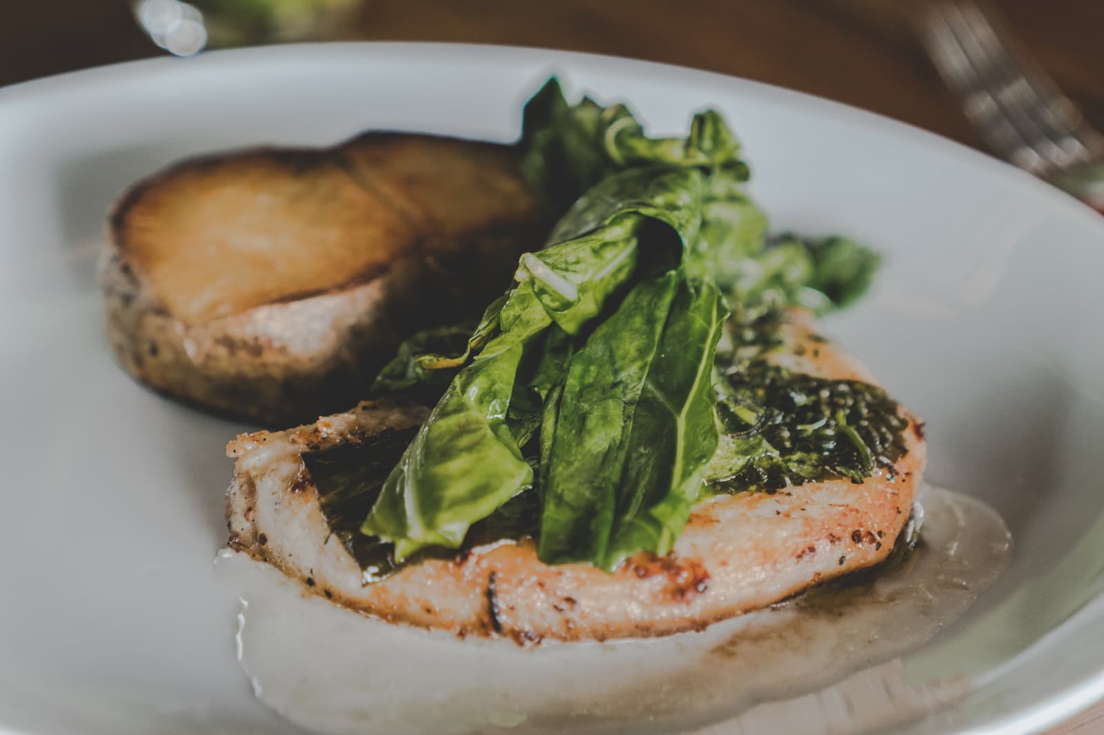 Simple ingredients, serious kitchen, lodge cooking that earns its own spotlight. Pan-seared fish fillet topped with fresh green leaves served on a white plate with a roasted portobello mushroom at a luxury Amazon lodge Brazil restaurant