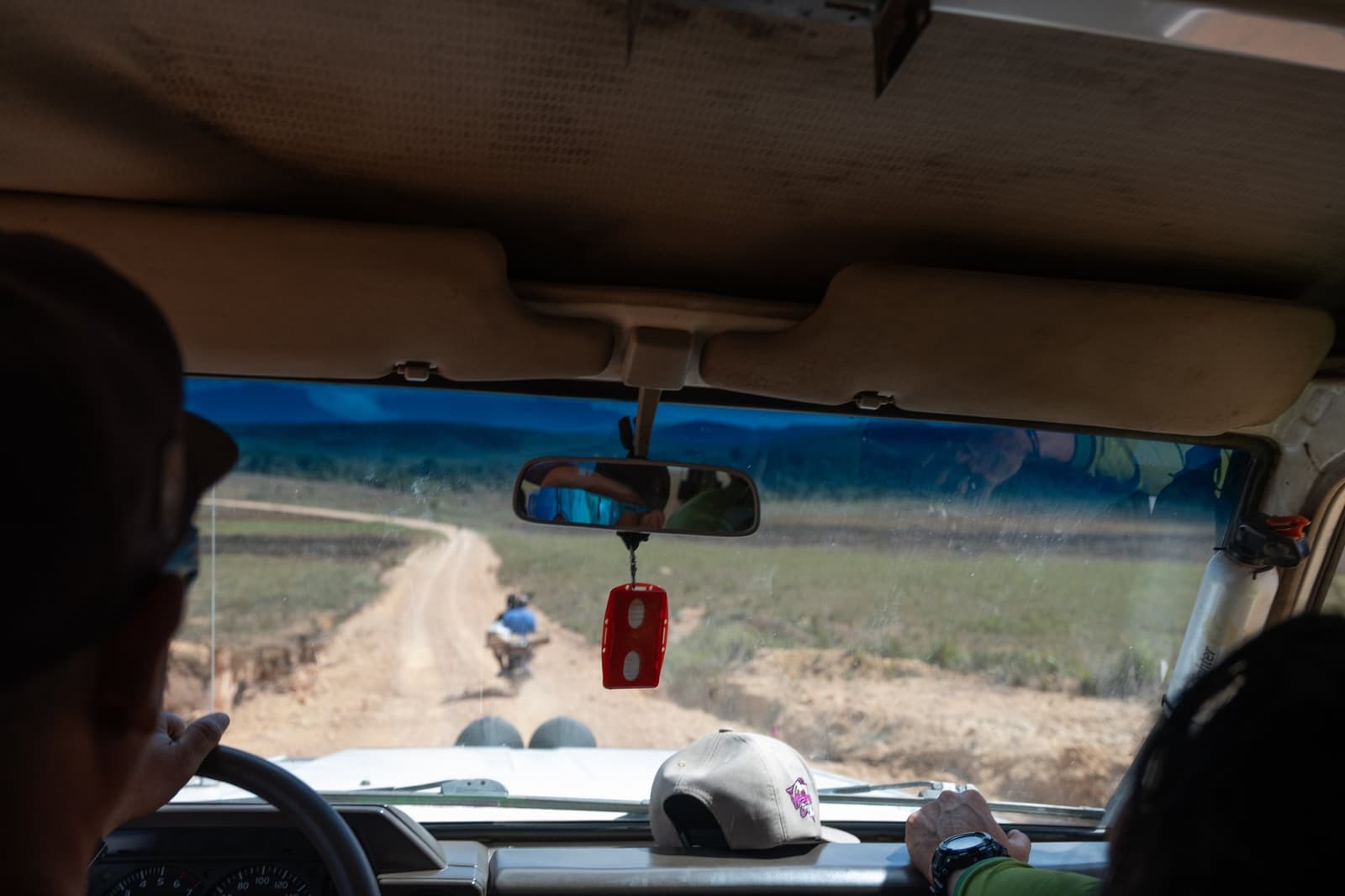 The adventure starts before you even leave the vehicle. View from inside a 4x4 vehicle following a motorcycle along a winding dirt road through open grassland on the Mount Roraima hike approach