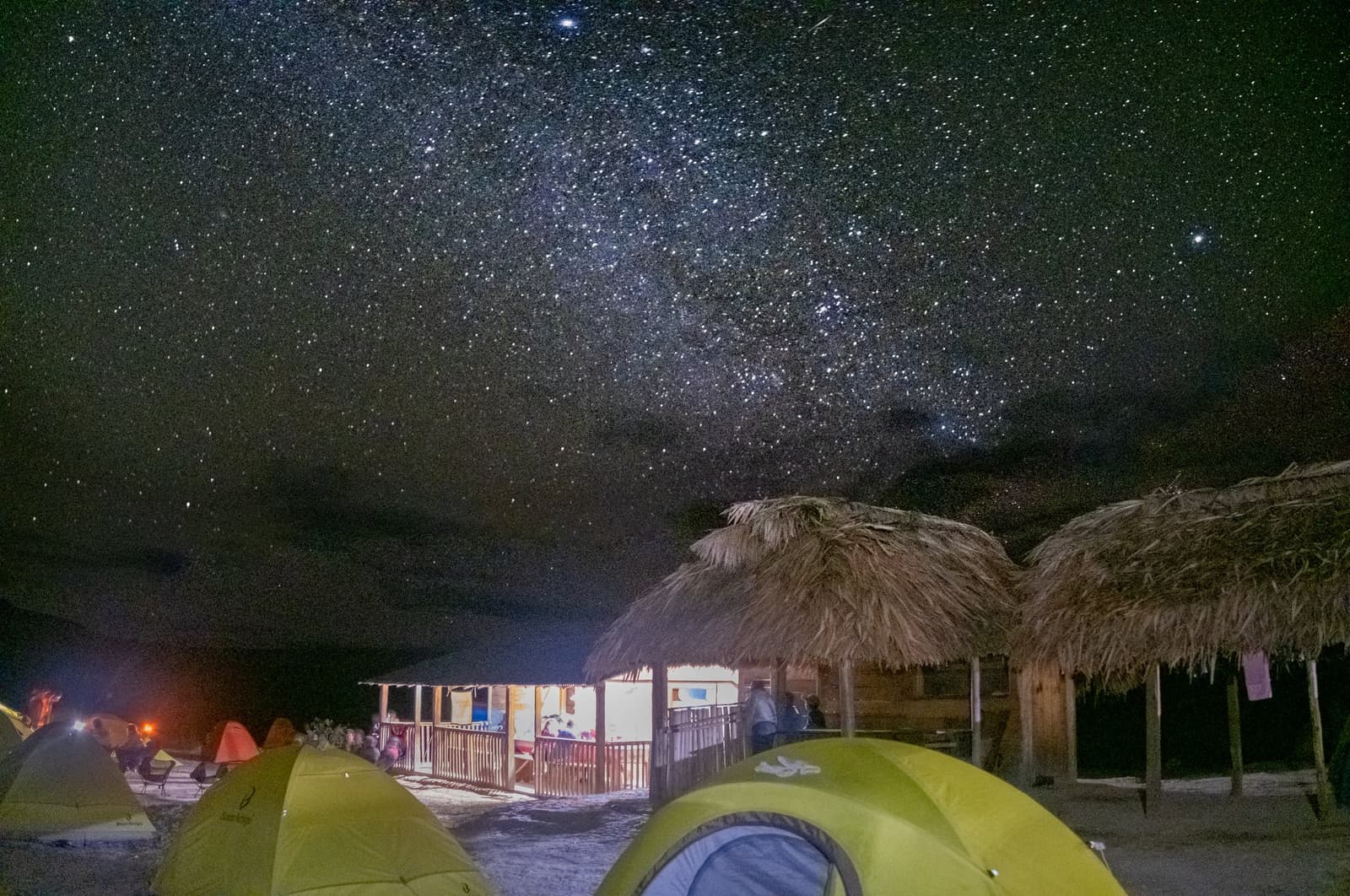 Dinner lights, thatched roofs, and half the galaxy overhead. Not a bad campsite. Green dome tents and thatched-roof shelters lit up at night on the Mount Roraima hike, with the Milky Way stretching across a dark sky above