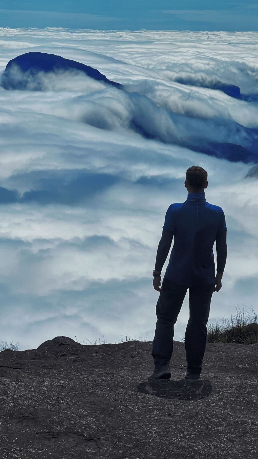 Up here, the clouds are the floor and the sky is yours. A hiker stands on the rocky summit plateau of the Mount Roraima trek, gazing out over a vast sea of clouds that swallows the surrounding tepuis below