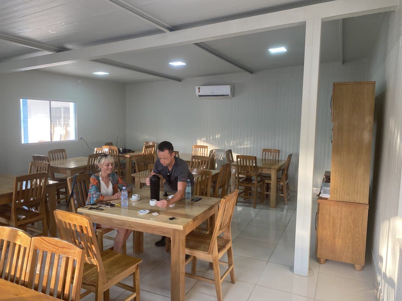 Good coffee and a quiet table, the perfect debrief after a morning on the water. Two travellers sharing coffee at a wooden table inside a clean, air-conditioned dining room on a pantanal jaguar budget safari