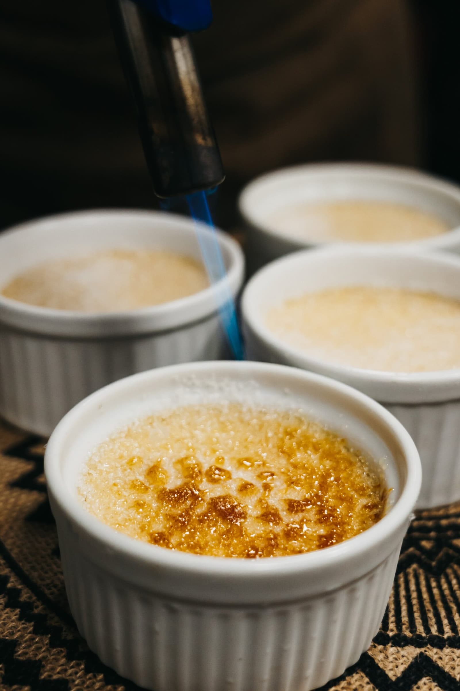 Yes, you get crème brûlée on a river in the middle of the jungle. A kitchen torch caramelising the sugar crust on a crème brûlée in a white ramekin, with three more unfinished ramekins in the background, served aboard the untamed amazon cruise