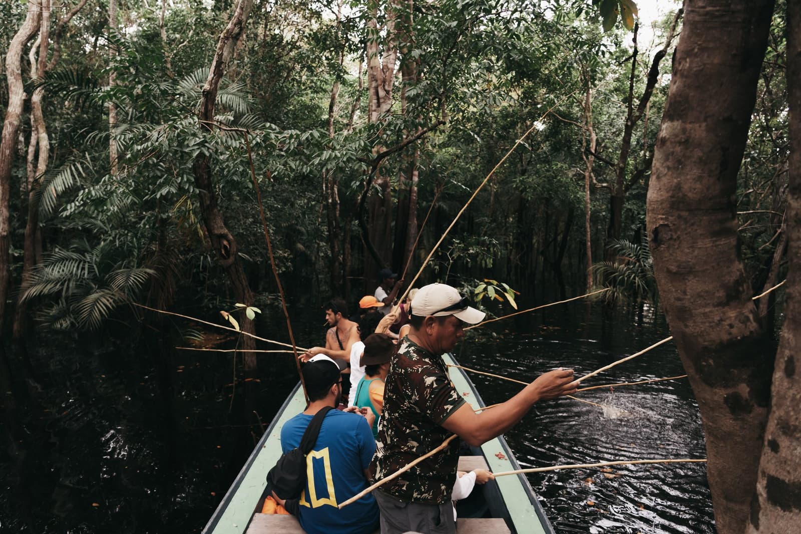 Everyone's a little competitive once the rods go in the water. A group of travellers fishing with bamboo rods from a narrow canoe on an untamed amazon cruise, surrounded by flooded igapó forest and dark black water