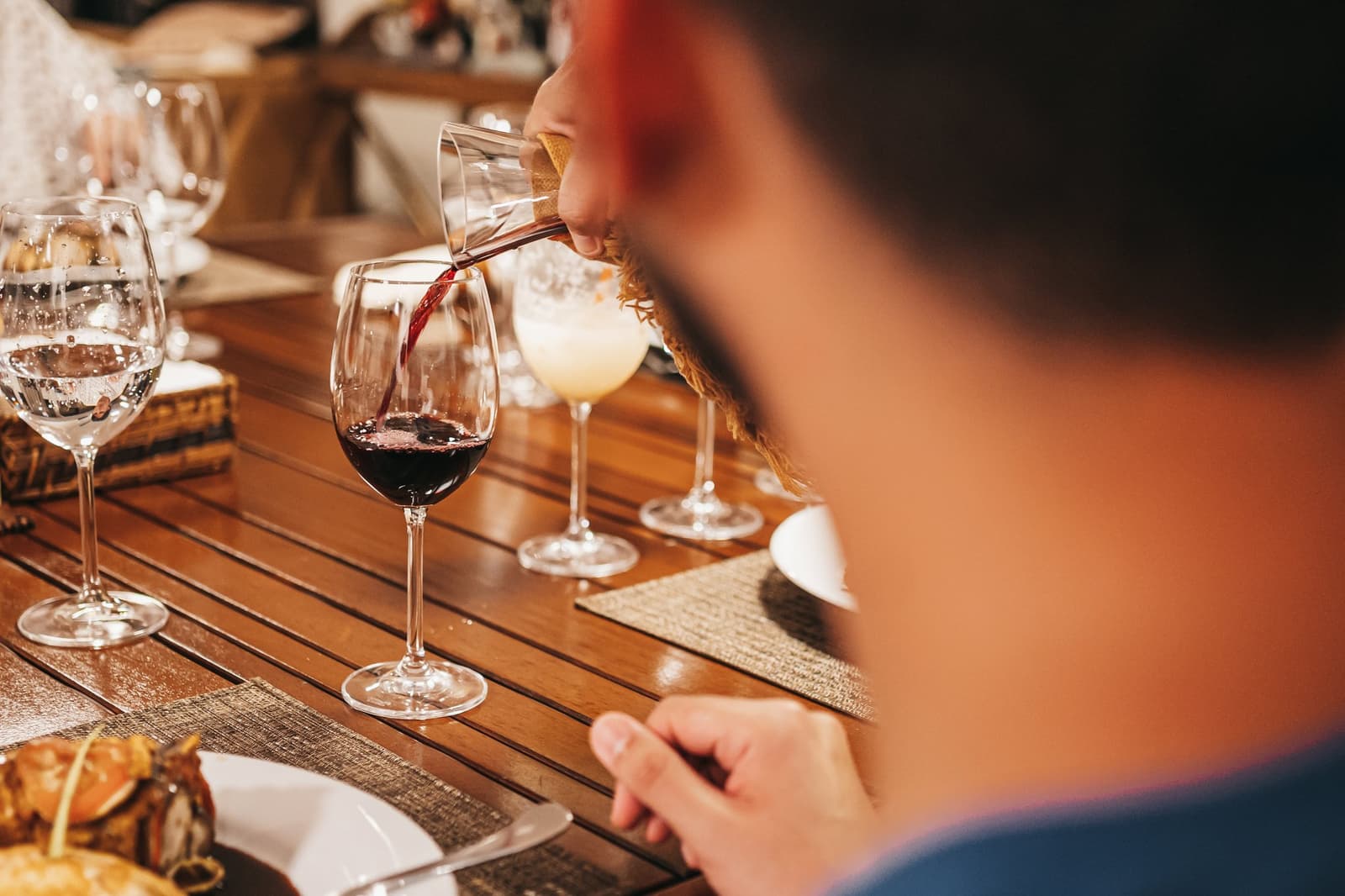 Good food, good wine, and the river just outside. Dinner on the Amazon earns its place. Red wine being poured into a crystal glass at a elegantly set dining table aboard the untamed amazon cruise, with cocktails and plated food visible alongside