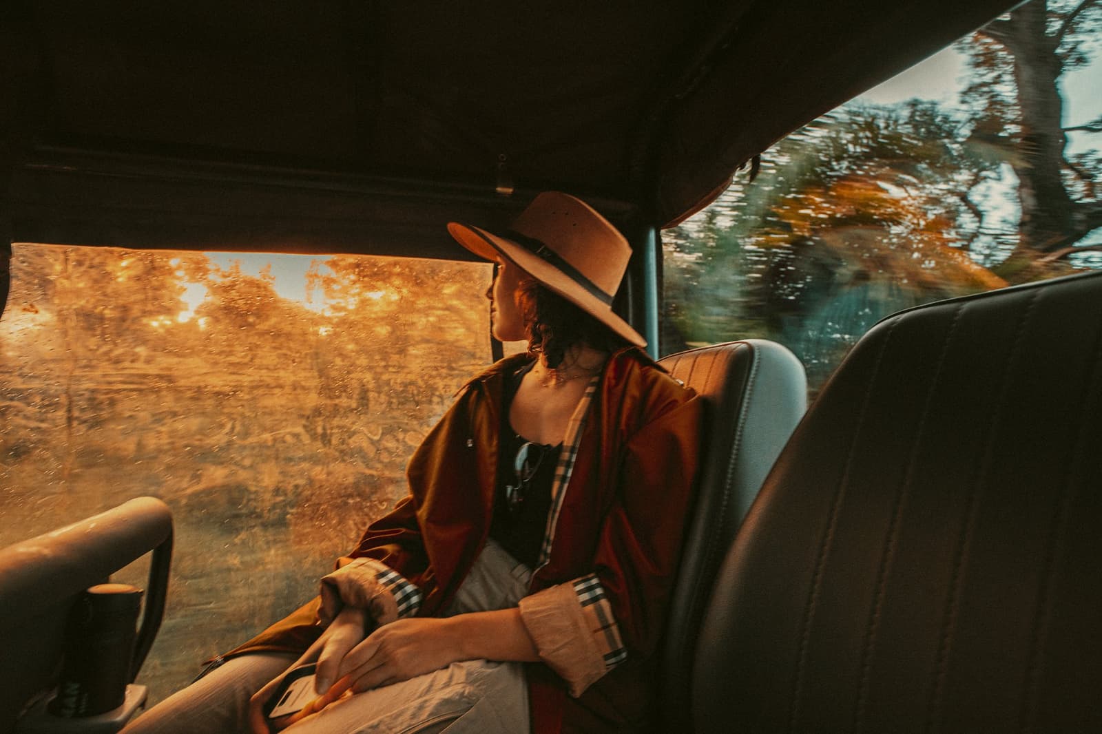Rain on the glass, gold on everything else, the transfer is already the trip. Photo: Felipe Castellari A traveler in a wide-brim hat and rust-colored poncho gazes out a rain-speckled 4x4 window during a luxury Pantanal and Amazon trip, golden light flooding through the glass as the vehicle moves through open wetland terrain