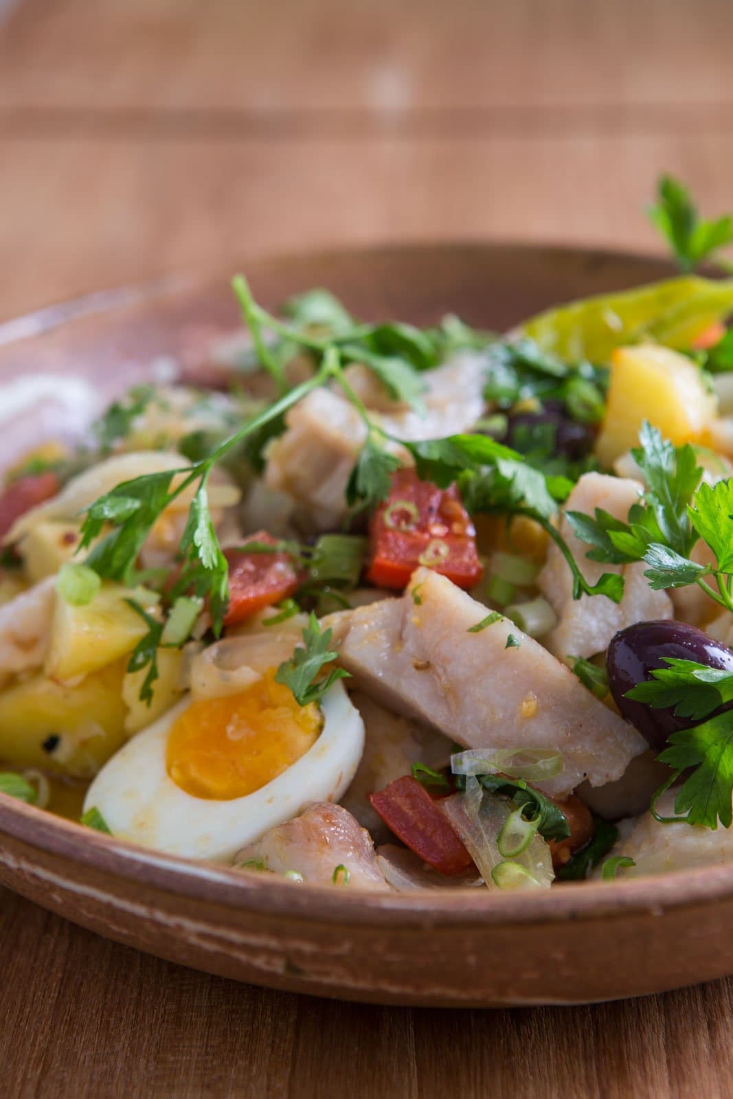 Comfort food with roots, served in the kind of bowl that tells you the cook means business. Photo: Rjcastilho A rustic clay bowl filled with flaked salted cod, boiled potato chunks, halved hard-boiled egg, dark olives, chopped parsley, spring onion, and diced red sausage, served on a wooden table during a luxury Pantanal and Amazon trip
