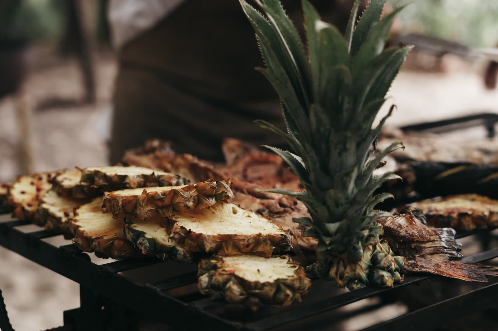 Fruit on the grill: not a garnish, the main event. Freshly cut pineapple halves and whole pineapple crown resting on an outdoor grill grate, caramelizing over an open fire as part of the full-board dining experience on a luxury Amazon cruise in Brazil