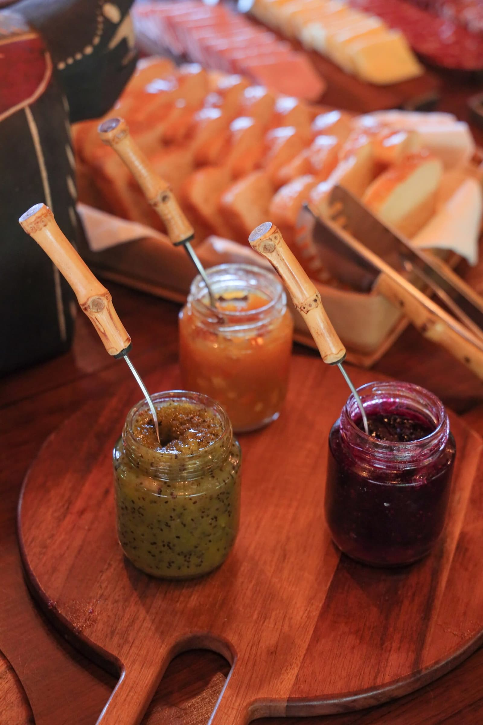 Three jars, three flavors, and a bread basket that makes leaving for the safari a little harder. Photo: thiagolbrito Three glass jars of artisan fruit jam with bamboo-handled spoons on a round wooden board, with sliced bread, papaya, and cheese arranged in the background on a lodge breakfast table during a luxury Pantanal and Amazon trip