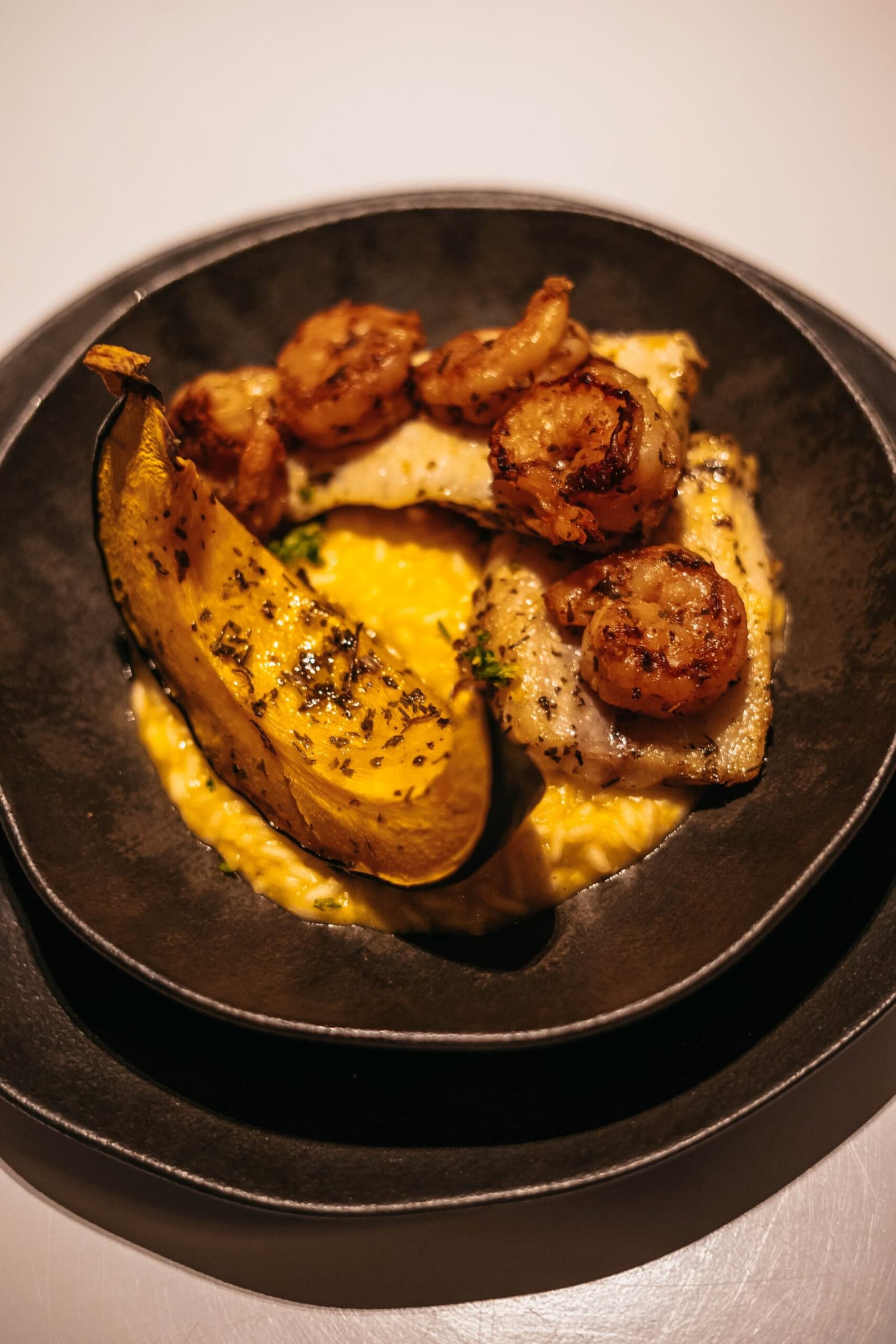Local ingredients, serious technique, river miles well earned. A dark cast-iron bowl on a luxury amazon cruise in brazil holds pan-seared shrimp, flaked white fish, a grilled plantain half, and a golden creamy sauce