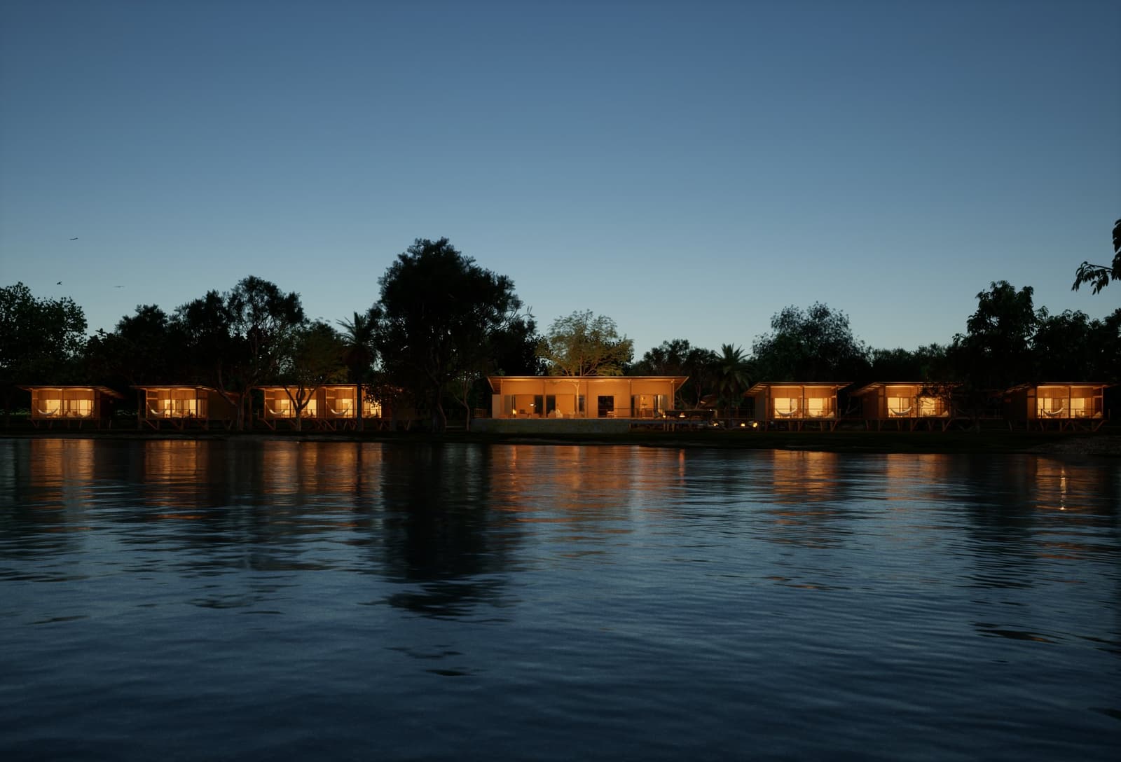 Come nightfall, the lodge glows like it has been expecting you. A row of warmly lit eco-lodge bungalows and a central pavilion reflected on a calm river at dusk, part of a luxury Pantanal and Amazon trip experience