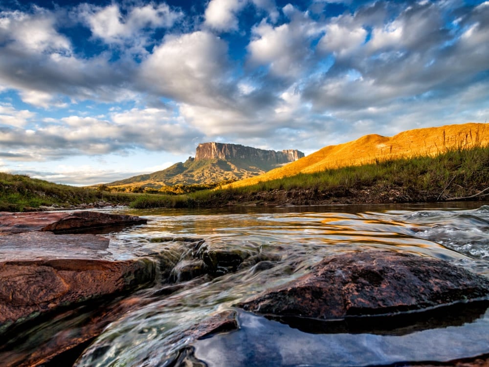 The Kukenán tepui next to Mount Roraima reflected in a river at golden hour The Kukenán tepui next to Mount Roraima reflected in a river at golden hour