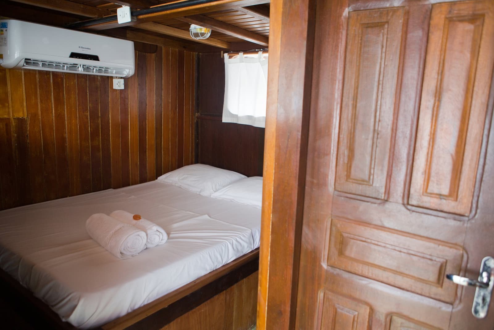 Snug quarters, cool air, and a river sliding past the window, not a bad way to sleep. Photo: sitah Cozy wood-panelled cabin on an amazon river cruise in Brazil, with a double bed, fresh white towels, a porthole window, and a wall-mounted air-conditioning unit