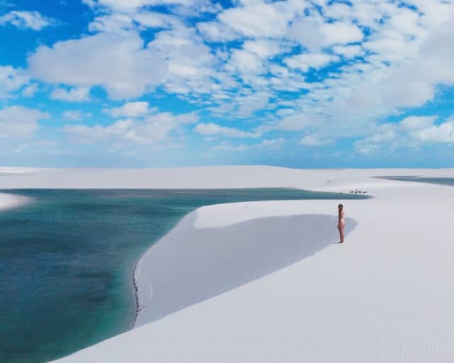 Woman standing on a white dune above a turquoise lagoon in Lençóis Maranhenses under a blue sky Woman standing on a white dune above a turquoise lagoon in Lençóis Maranhenses under a blue sky
